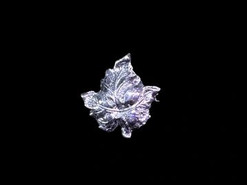 A close-up of a metallic leaf sculpture against a black background.