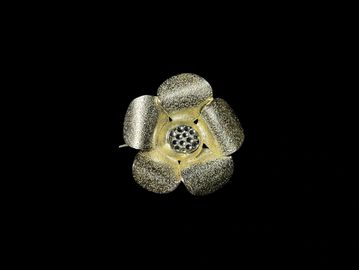 A metallic flower brooch with a black gemstone center.