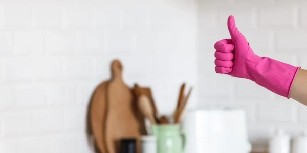 Hand in pink glove giving thumbs up in a clean kitchen.
