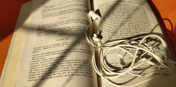 White earphones tangled on an open book under warm sunlight.