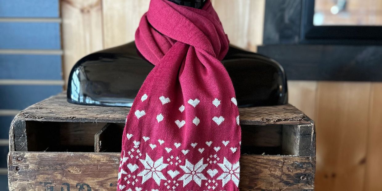 Red scarf with white hearts and snowflakes draped over a black mannequin on a wooden crate.