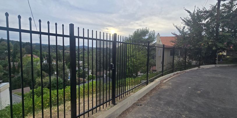 Black metal fence along a curved driveway overlooking a scenic view.