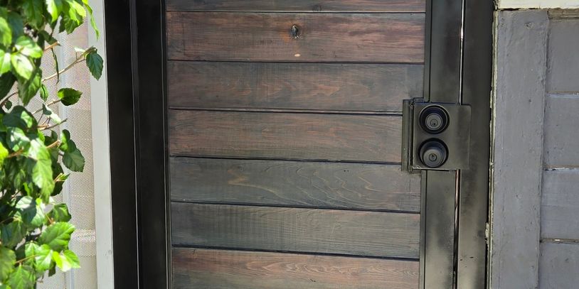 Modern wooden gate with black metal frame and lock.