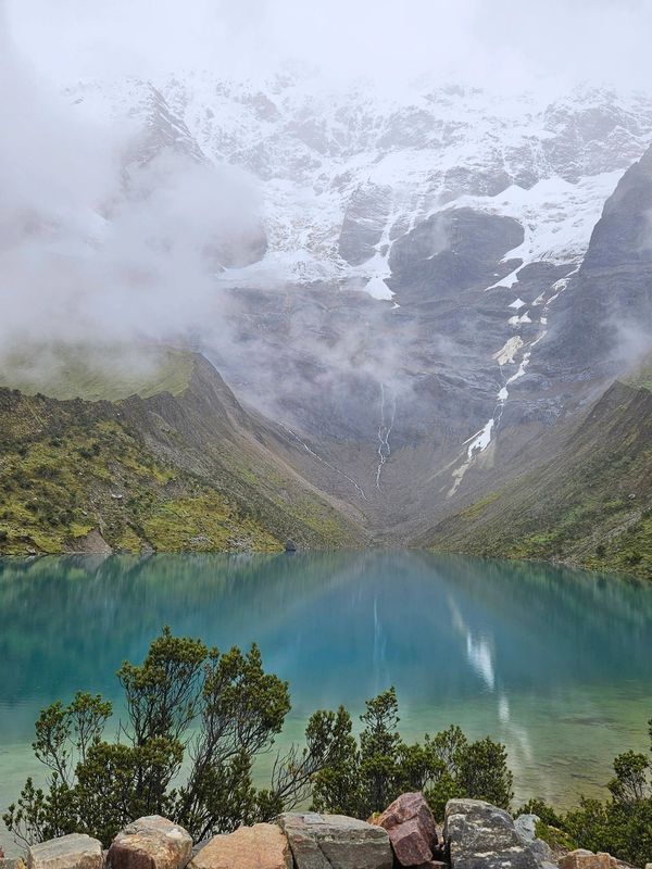 Serene mountain lake with snow-capped peaks and misty clouds.