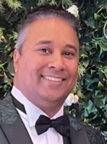 Smiling man in a tuxedo with a floral background.