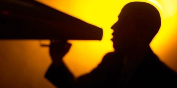 Silhouette of a person speaking into a megaphone against a warm yellow background.