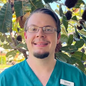 Smiling healthcare worker in teal scrubs outdoors.