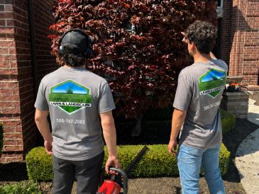 Two lawn care workers in branded shirts working in a yard.