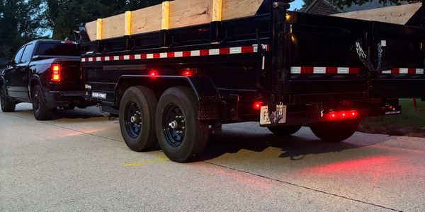 Black truck towing a black flatbed trailer with wooden sides.