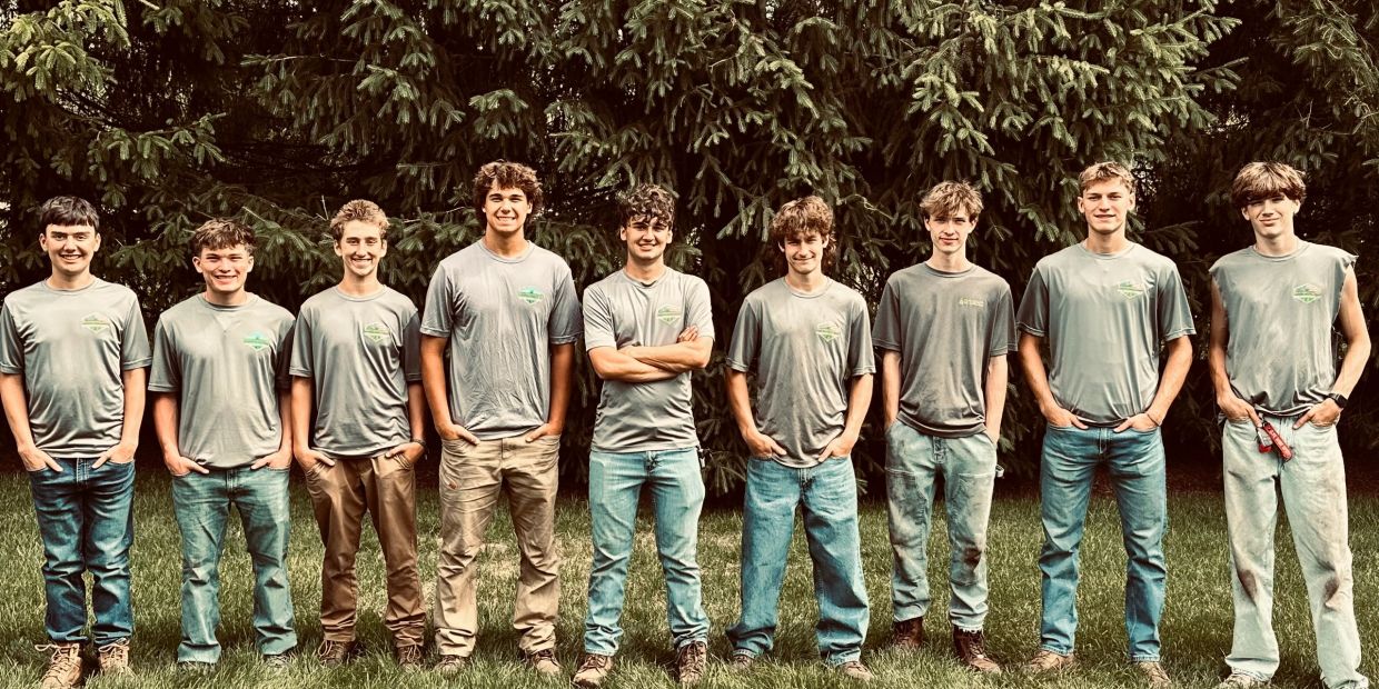 Group of ten young men standing outside in matching shirts.