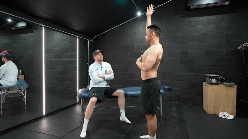 Coach observing athlete stretching in a gym.