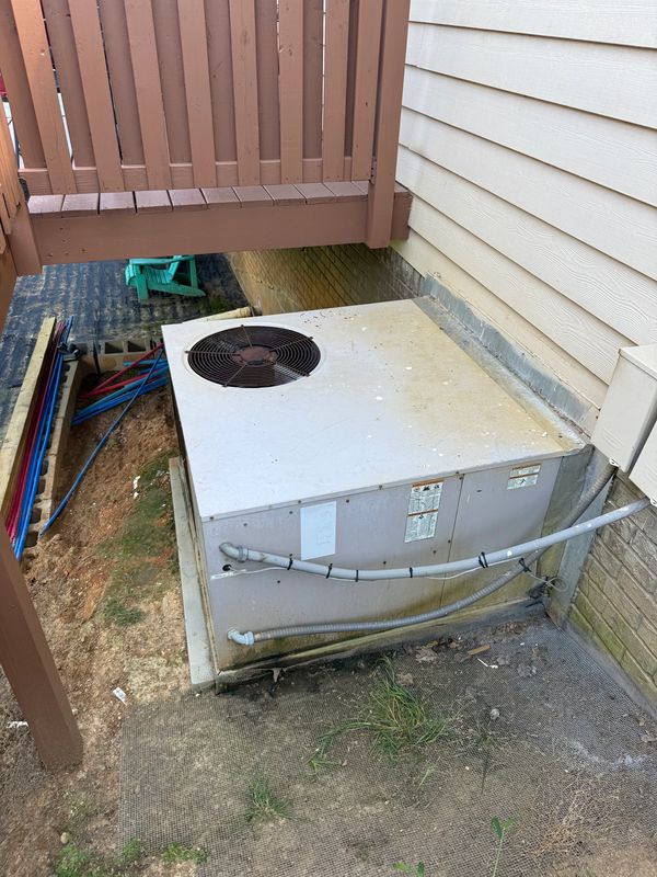 Outdoor HVAC unit installed beside a house under a wooden deck.
