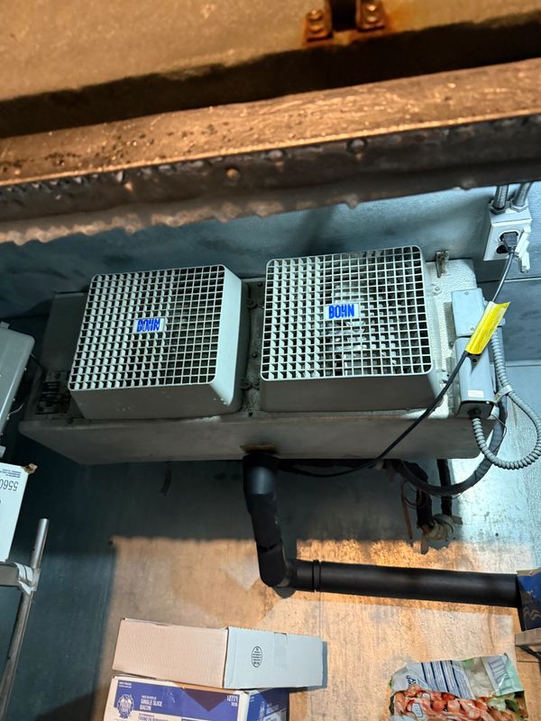 Two industrial ventilation units mounted on a wall above boxes and pipes.