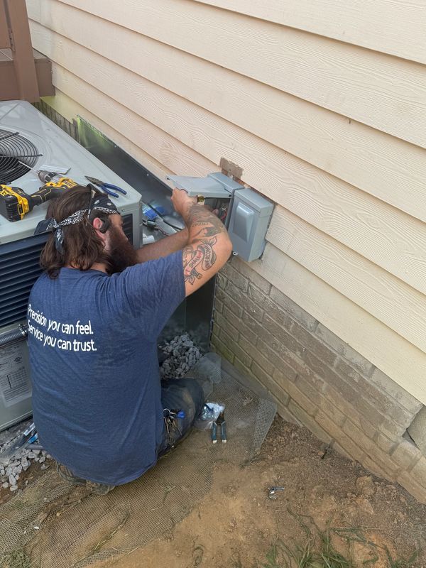 Technician fixing an outdoor electrical box near an HVAC unit.
