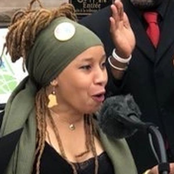 Dr. Lindo excited as she speaks at a microphone. Hands are clapping behind her as she speaks.