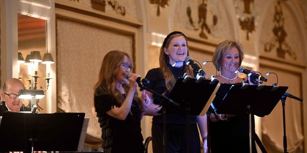 three women in black attire are singing 