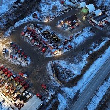 Aerial view of a snowy industrial yard with parked trucks and equipment near a road.