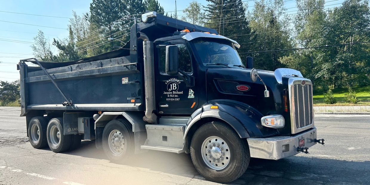 Black dump truck parked on a road near trees on a sunny day.