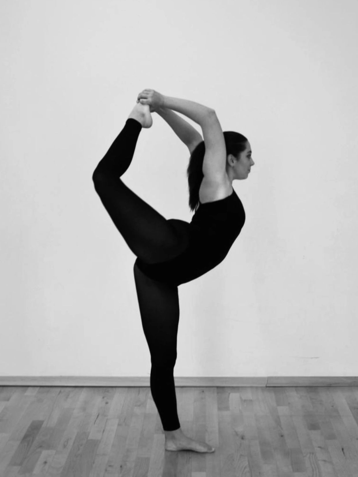 Woman in black outfit balancing in a yoga pose against a plain background.