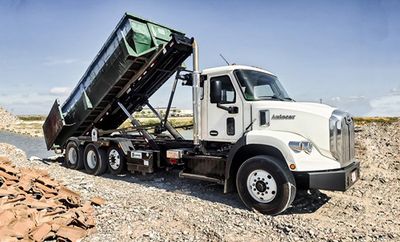 White dump truck unloading rocks on a gravel site under a clear sky.