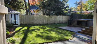 Sunny backyard with green lawn and wooden deck area.