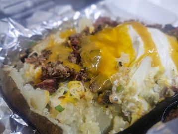 Baked potato topped with melted cheese, sour cream, and chopped meat on foil.