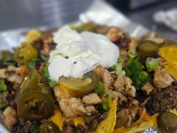 Loaded nachos topped with jalapeños, sour cream, and mixed meats.