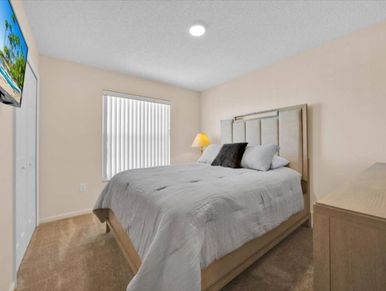 Simple, cozy bedroom with a bed, lamp, and TV.