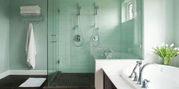 Modern bathroom with glass shower and bathtub, featuring soft green walls and white accents.