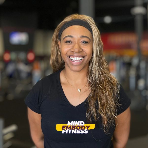 "Black woman with warm smile and long wavy blonde hair, wearing a black Mind Embody Fitness Shirt.