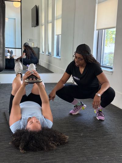 A Black Female Trainer guides a woman lifting a kettlebell during a workout session.
