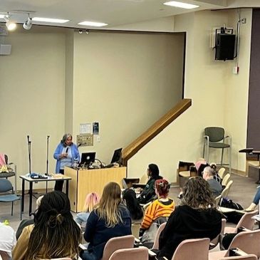 A woman giving a lecture to an audience in a classroom.