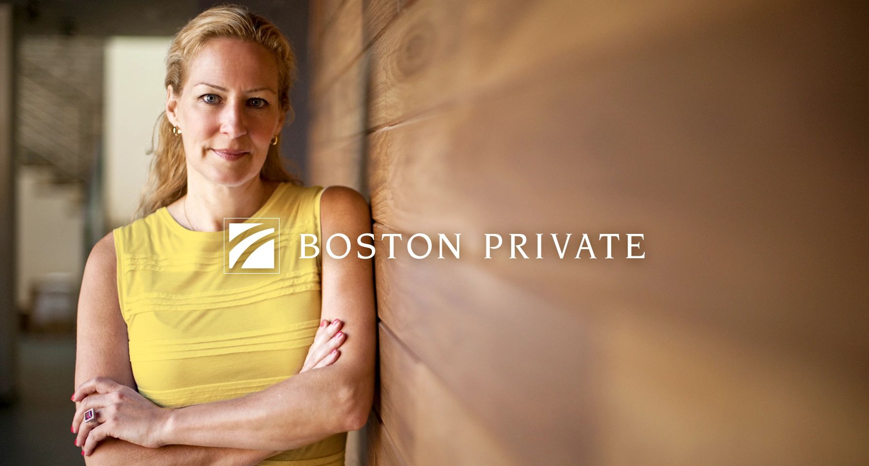 A confident woman in yellow stands against a wooden wall with Boston Private logo.