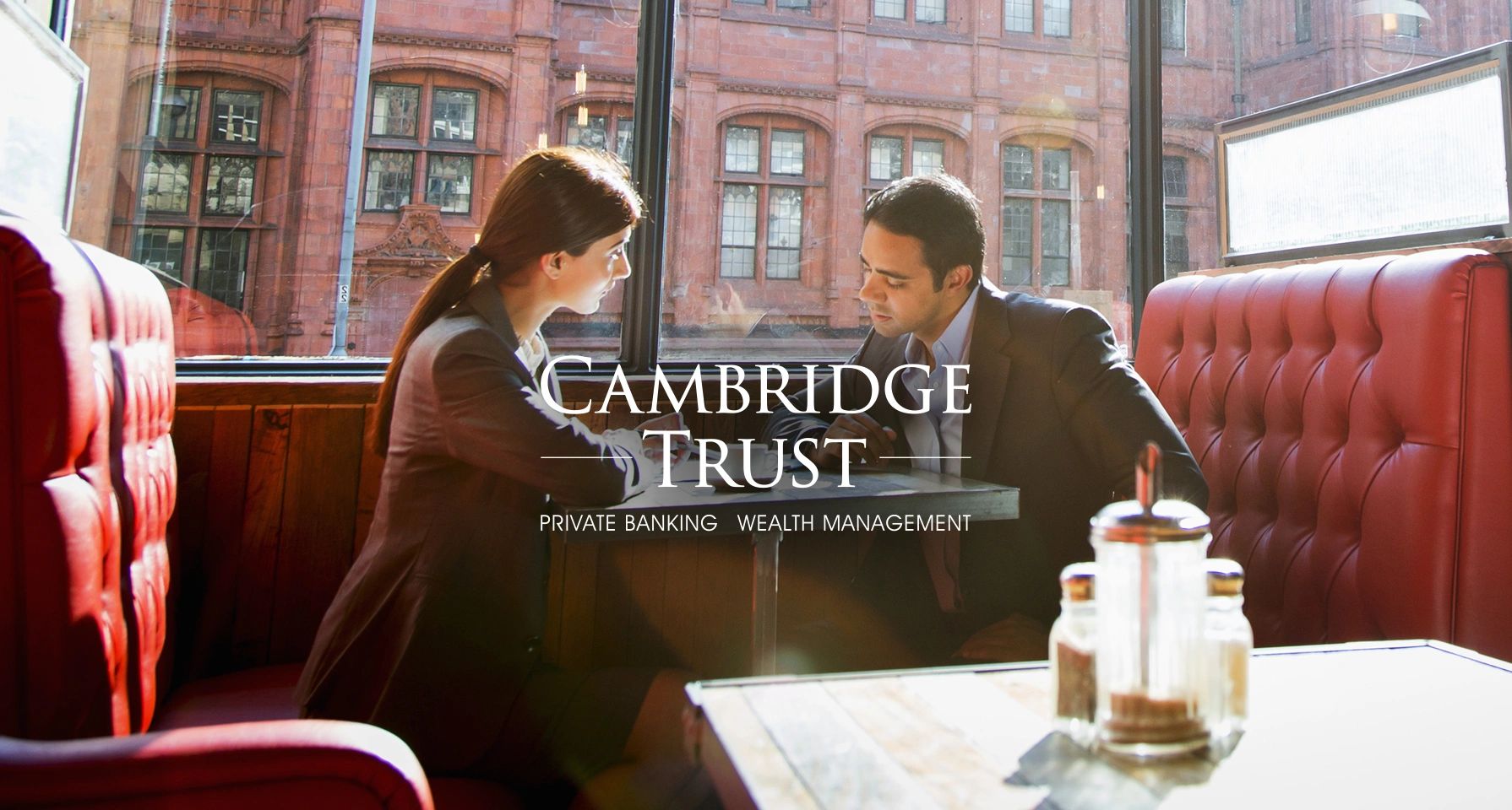 Two professionals discussing at a cafe booth with Cambridge Trust branding.