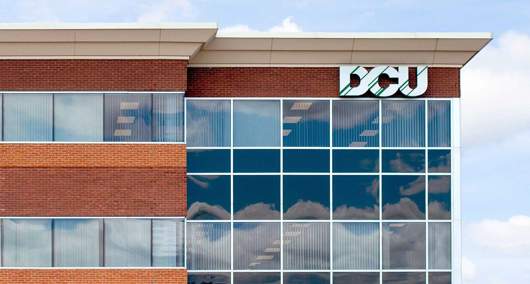 DCU building with glass windows reflecting clouds.
