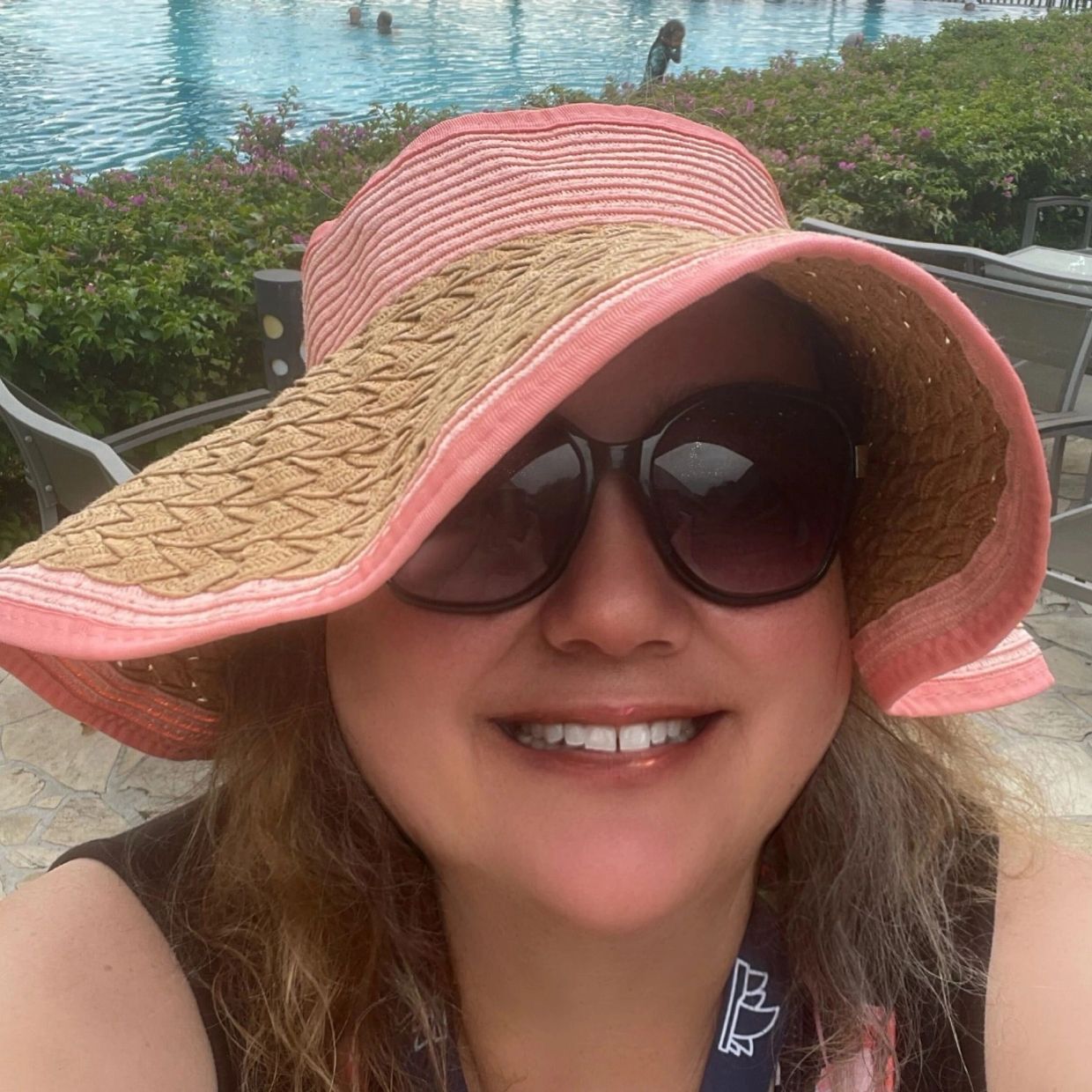 Woman in sunglasses selfie image.  Pool in background and black sand 
Tahitian beach behind the pool