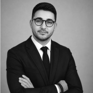 Professional man in black suit with glasses posing confidently.