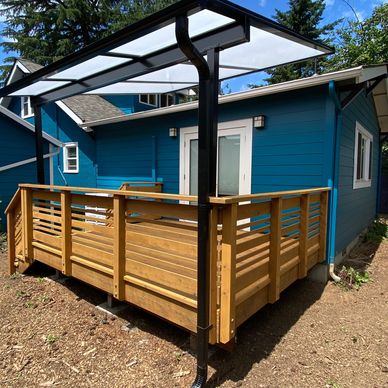 Wooden deck with railing and transparent roof attached to a blue house.