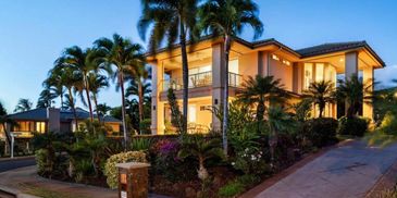 Luxurious two-story house surrounded by palm trees.