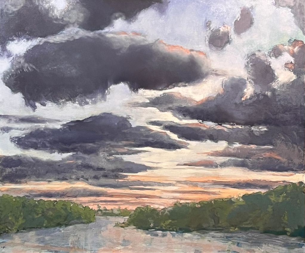 A dramatic sky with dark clouds over a river and green trees at sunset.