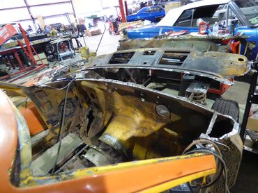 Rusty and dismantled car body inside a garage with classic cars in the background.