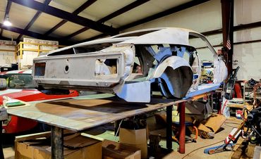 A stripped classic car body on a workbench inside a garage.