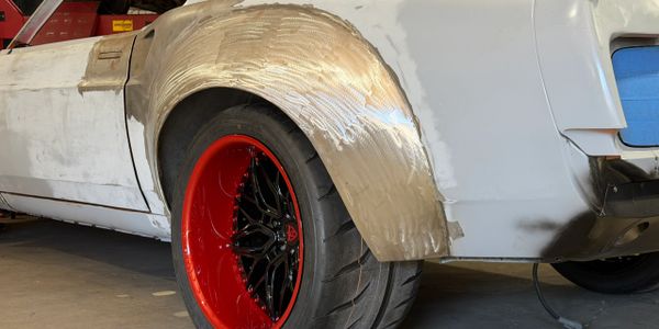 Close-up of a car's rear wheel with a custom metal fender and red-black rim.