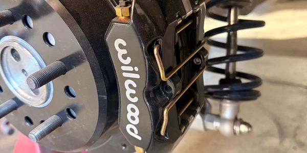 Close-up of a Wilwood brake caliper and suspension spring on a vehicle.