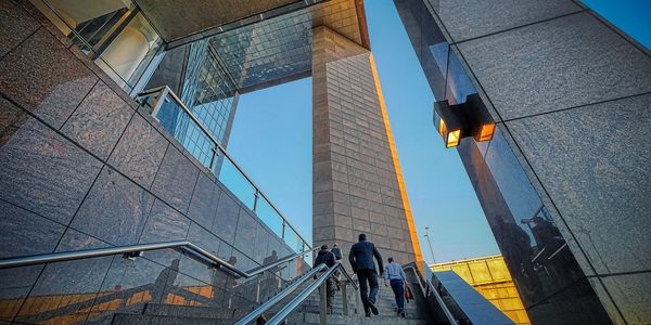 People ascending stairs within a modern urban building with reflective glass walls.
