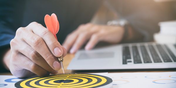 Hand holding a dart aiming at the center of a yellow and black target.