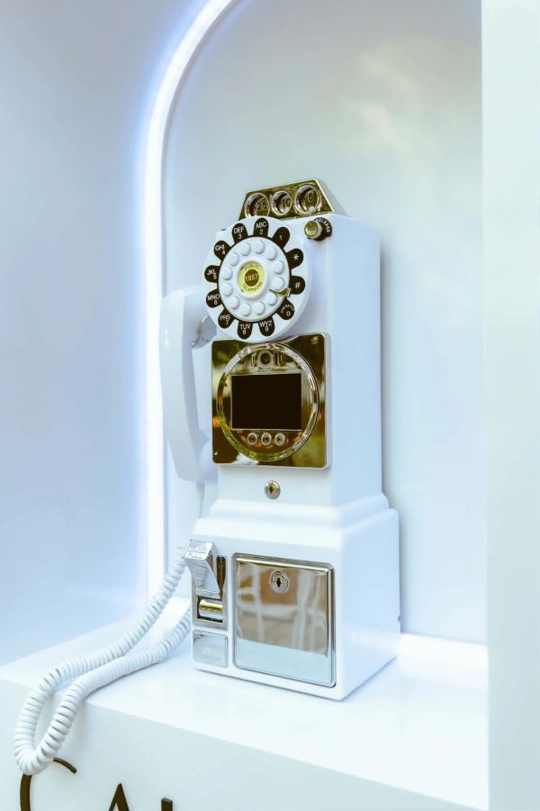White vintage rotary dial payphone with gold accents.