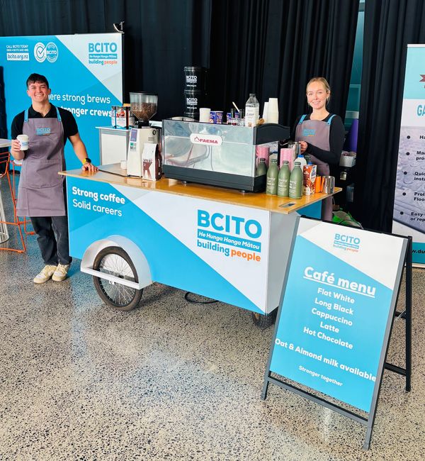 Two of our baristas smiling at a coffee cart with BCITO branding.