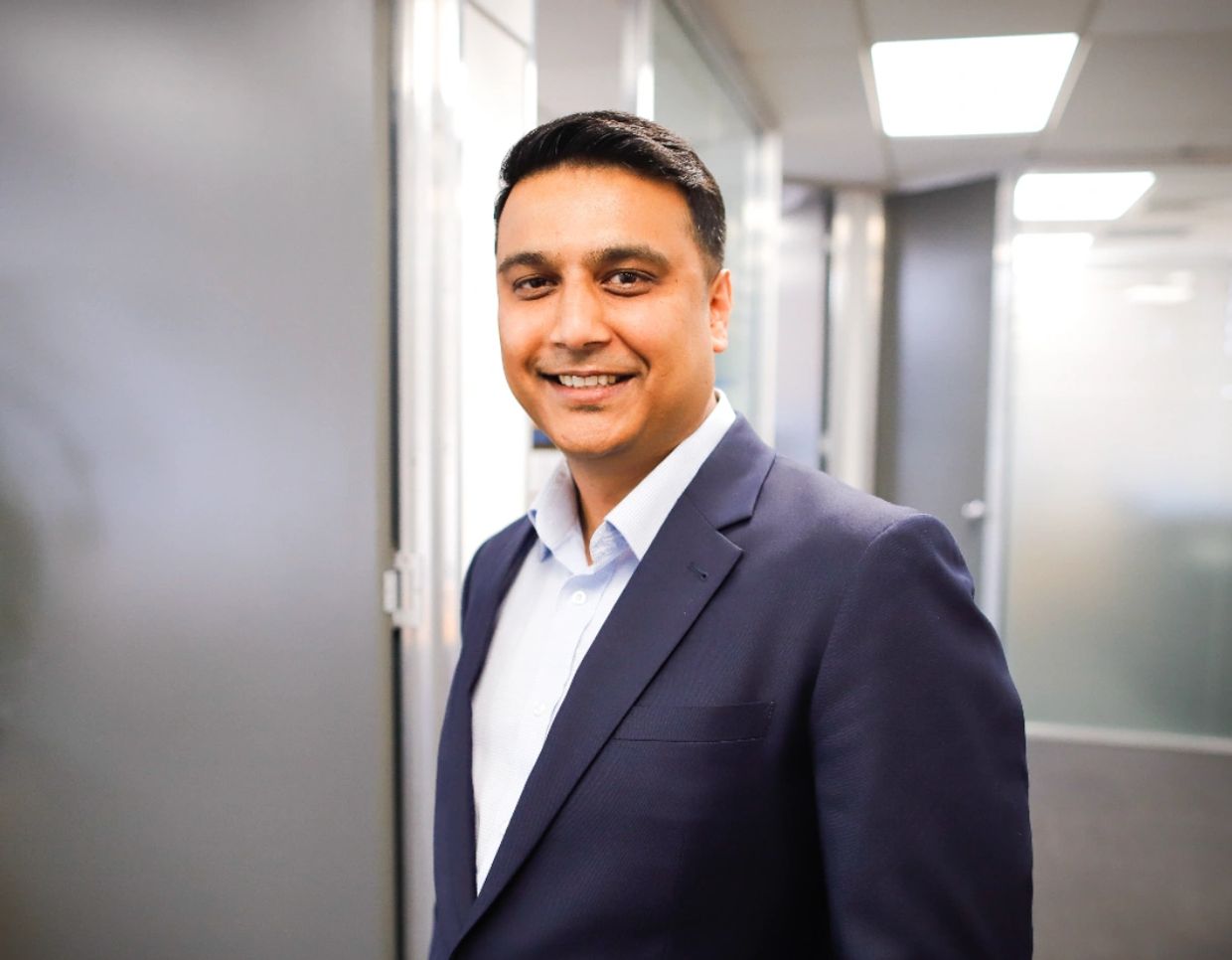 Smiling man in a navy blue suit standing in a modern office.