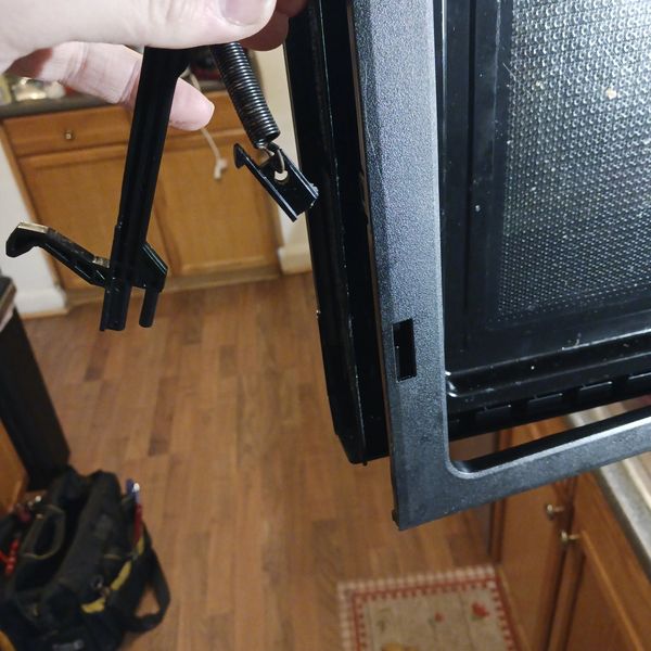Hand holding oven door spring and latch mechanism.